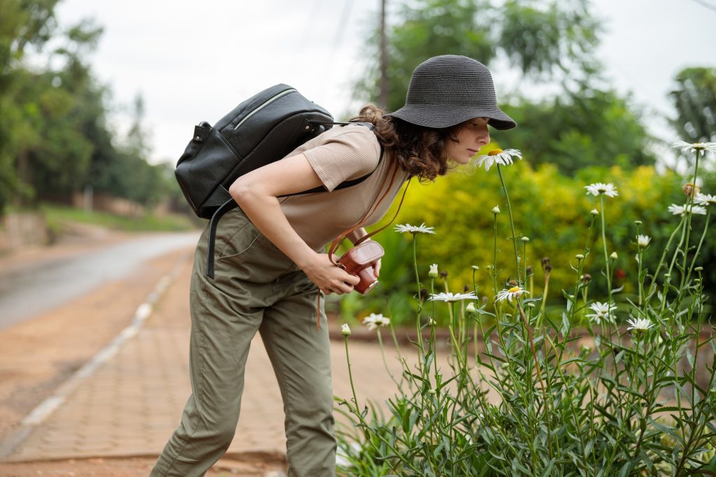 Pretty woman with backpack smelling flowers outdoors